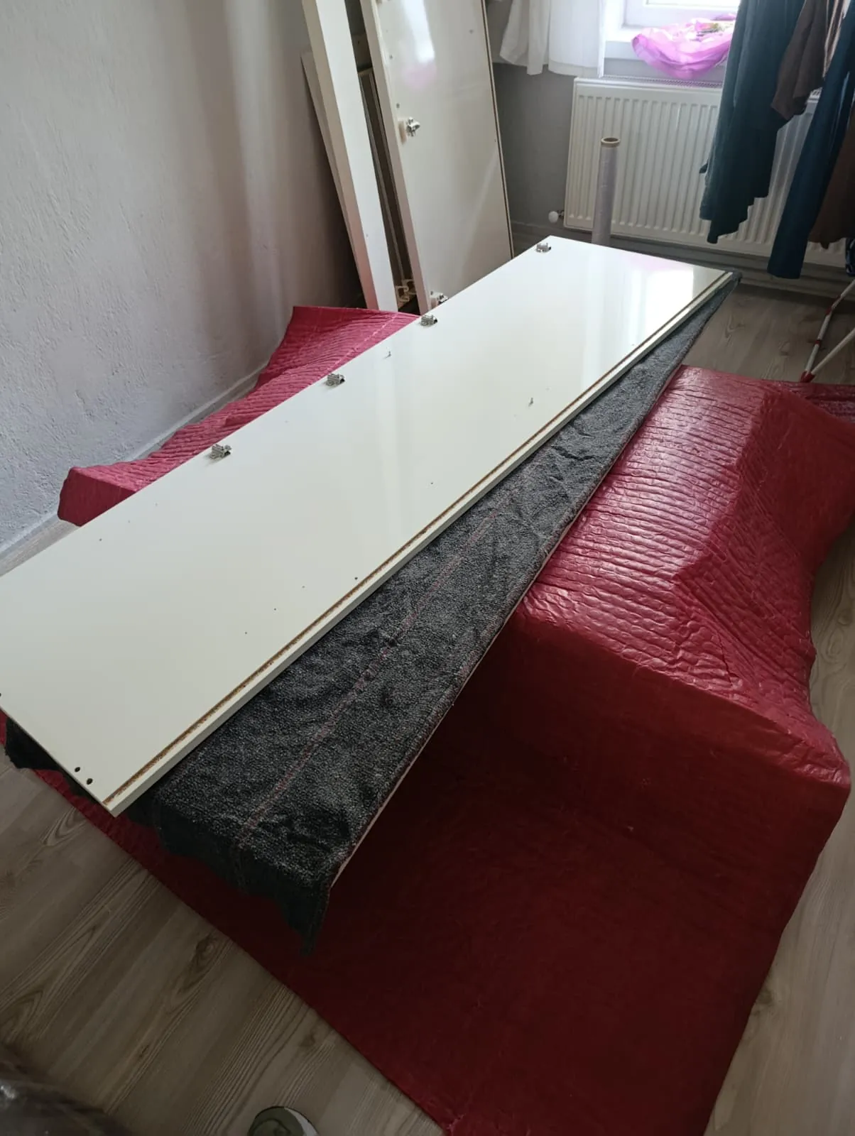 Menteşeli beyaz gardırop kapağı, kırmızı örtülü gövde üzerinde.