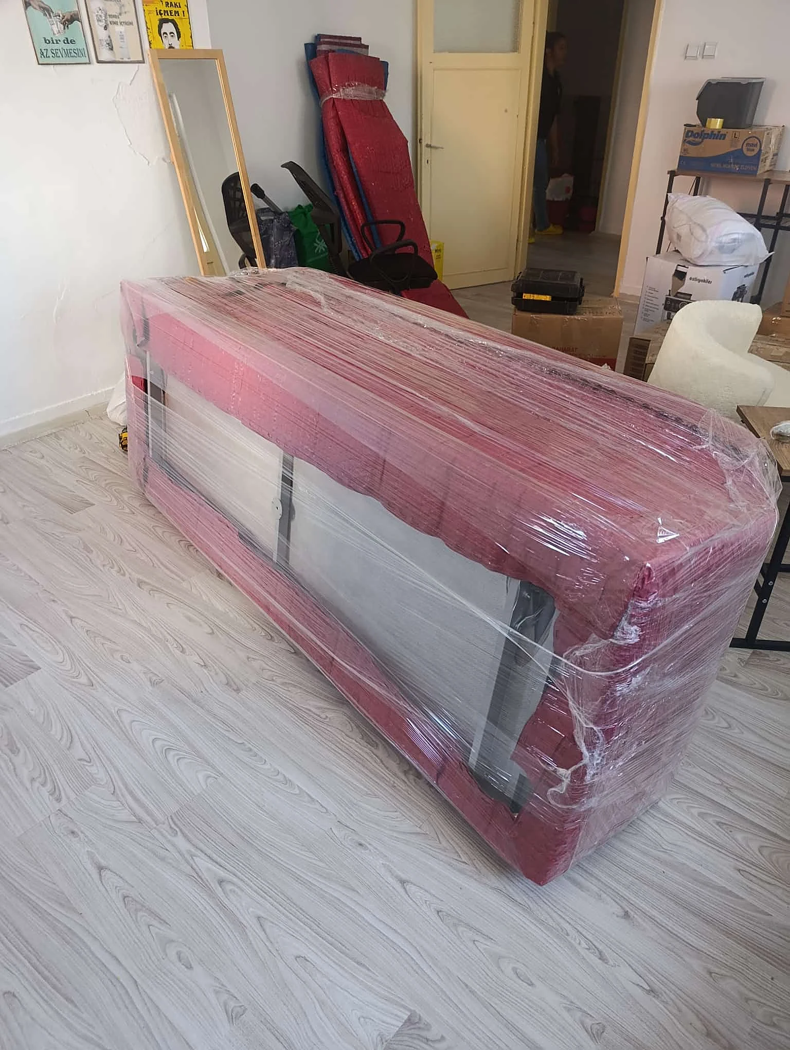 Kırmızı örtülü paketli koltuk, ayna ve karton kutular yanında.
