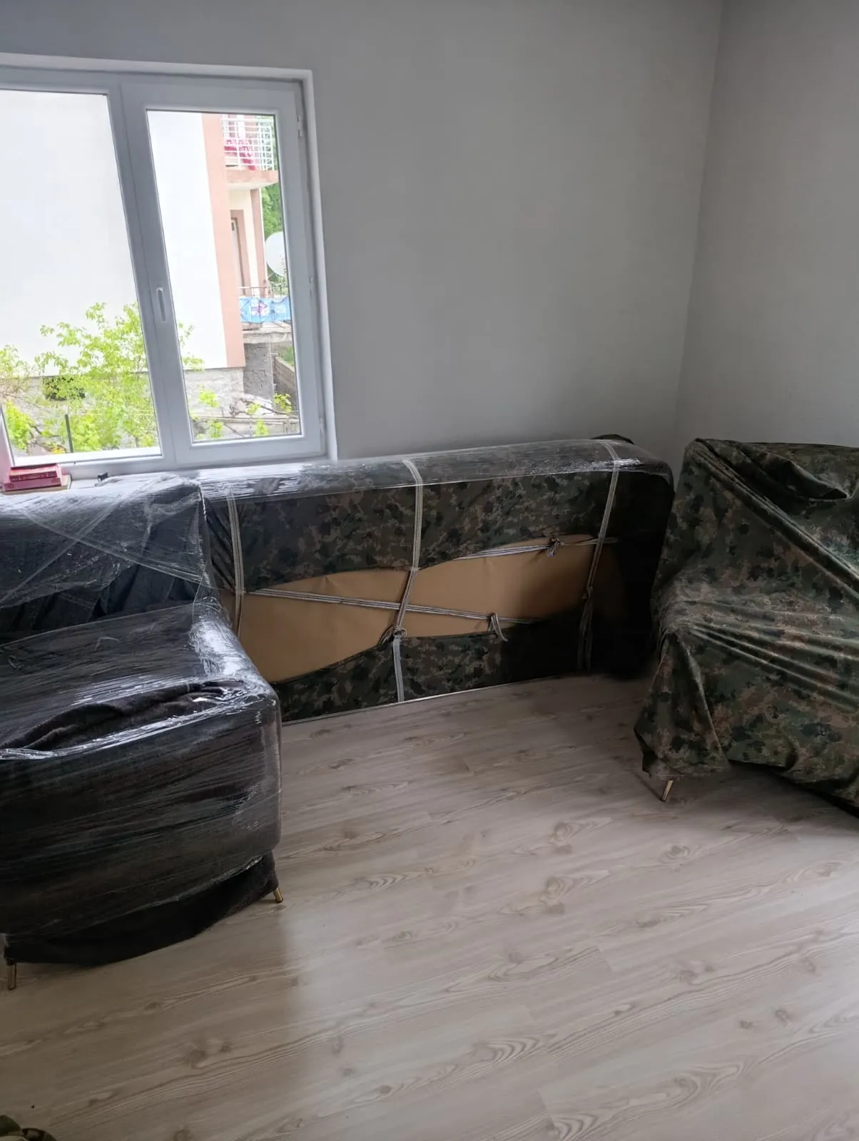 Streç filmli berjer ve kamuflaj örtülü koltuk, odada paketli.