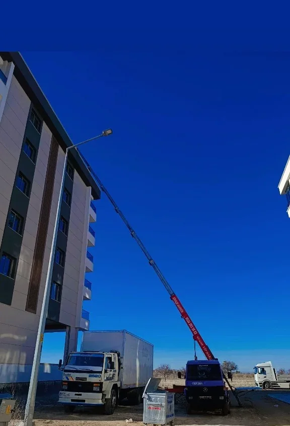 Yavuzlar kiralık asansör vincinin apartman cephesine uzandığı taşıma anı; yanında kapalı kasa nakliye kamyonu.